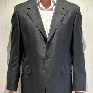 Grå vintage kavaj från Yves Saint Laurent - Elegant Yves Saint Laurent-kavaj i storlek 54. Tillverkad av bomull och silk med en lining av rayon. En tidlös design med fina detaljer, skräddarsydd passform och YSL:s ikoniska elegans och kvalitet. Den korrekt färgen är den som syns i bild två, ljuset blev lite konstigt i de andra bilderna. 