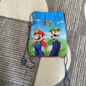 Super Mario ryggsäck - Cool Super Mario ryggsäck med motiv av Mario och Luigi. Väskan har en blå framsida med färgglada detaljer och en röd baksida. Perfekt för att bära med sig det viktigaste på ett lekfullt sätt.