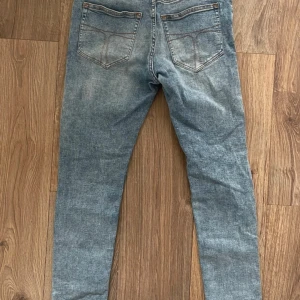 Blåa tiger of Sweden jeans 30/31 - Snygga blå jeans med en klassisk femficksdesign och en läderdetalj vid midjan. De har en normal passform och är perfekta för en avslappnad stil. Jeansen har en lätt tvättad look som ger dem en trendig touch.