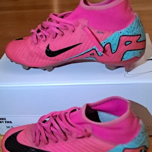 Str 36,5 Nike Mercurial fotbollsskor i rosa och turkos - Säljer ett par Nike Mercurial fotbollsskor i en snygg rosa färg med turkosa och svarta detaljer. Skorna har snörning och är tillverkade i syntetmaterial med NikeSkin-teknologi. Perfekta för dig som vill sticka ut på planen!