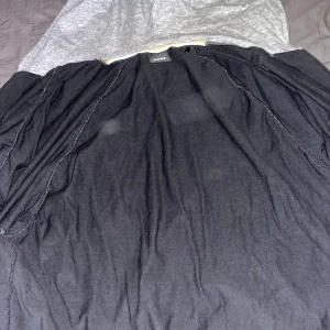 Svart lång jacka med huva från Hugo Boss - Säljer en svart lång jacka från Hugo Boss med huva och diskreta vita detaljer längs sömmarna. Jackan har en stilren design och är perfekt för dig som gillar en enkel men snygg look. Märkt med 'Better Boss'.