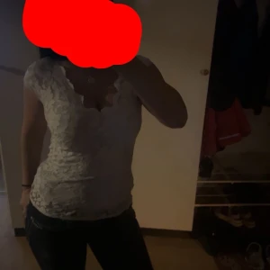 Vit spetsblus med v-ringning - Säljer en vit blus i spets med djup v-ringning och korta ärmar. Blusen har en feminin och figurnära passform, perfekt att styla till jeans eller kjol. Spetsdetaljerna ger en romantisk känsla.