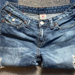 Blå bootcut jeans från True Religion - Säljer ett par blå jeans från True Religion med bootcut passform och slitna detaljer på benen.                                         Midjemått:37 cm   Inerbensmått:78 cm.  Midjehöjd:19 cm skriv gärna prisförslag!!!!!!!!! ordinarie pris 2229