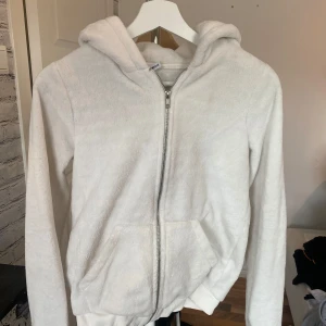 Vit fleece hoodie från Gina Tricot - Mysig vit hoodie från Gina Tricot i storlek S. Tröjan är tillverkad i mjuk fleece, har huva, dragkedja framtill och två praktiska fickor. Perfekt för chill dagar och när du vill ha något extra bekvämt. Långärmad och med ribbade muddar vid ärmslut och nederkant.