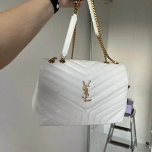 Vit quiltad axelväska från Saint Laurent - Säljer en snygg vit axelväska från Saint Laurent med guldiga kedjor och YSL-logga framtill. Väskan är quiltad i ett V-mönster och har en praktisk dragkedja inuti. Tillverkad i mjukt skinn och har en stilren, lyxig look som verkligen sticker ut. Vid snabb affär kan jag gå ner i pris. Ver inte om den är äkta. 