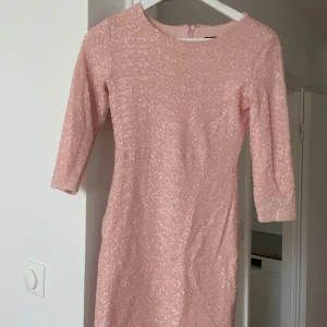 Ljusrosa paljettklänning TFNC London - Säljer en ljusrosa paljettklänning från TFNC London köpt på Nelly. Klänningen har trekvartsärm, rund hals och dragkedja i ryggen.