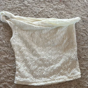 Offshoulder spets tubtopp i vitt - Säljer en vit offshoulder tubtopp med vacker spets och blommigt broderimönster. Toppen har en unik omlott-detalj upptill och är perfekt för dig som gillar romantisk och feminin stil. Passar snyggt till jeans eller kjol för en trendig look. 