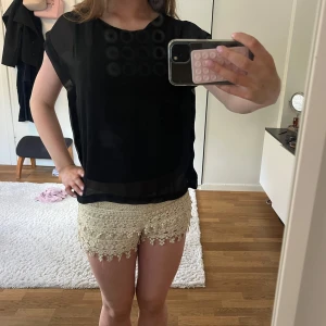 Svart blus  - Säljer en svart blus med meshpartier på axlar och ärmar. Blusen är tillverkad i ett lätt, syntetiskt material. Perfekt för dig som gillar stilrena och enkla plagg med en twist. 