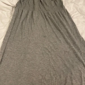 Grå långklänning med spets från Serenity - Snygg grå långklänning från Serenity med tunna axelband och vit spetsdetalj längs både överdelen och nederkanten. Klänningen är gjord i mjukt material med 70% viskos, 29% polyamid och 1% elastan. Perfekt för dig som gillar en enkel men romantisk look.