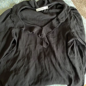 Svart blus med volang från Carin Wester - Säljer en svart blus från Carin Wester i storlek 34. Blusen har lång ärm och en snygg volangdetalj längs halsringningen som ger en cool touch. Materialet känns mjukt och har ett lätt fall. Perfekt för dig som gillar stilrena plagg. Hör av dig vid frågor!💕
