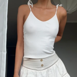 Vit ribbad linnetopp med knytband - Supersöt vit linnetopp med smala axelband som knyts på axlarna. Toppen är ribbad och har en v-ringad halsringning. Perfekt för varma dagar och enkel att matcha med allt. Materialet känns mjukt och lätt mot huden.