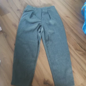 Grå kostymbyxor från Topshop Petite - Snygga grå kostymbyxor från Topshop Petite i storlek 34. Byxorna har rak passform, pressveck fram och bälteshällor i midjan. Materialet är mjukt och känns som en blandning av polyester och bomull. Perfekt för en clean och stilren look.