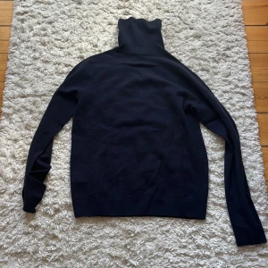 Mörkblå/svart Kashmir polotröja från Uniqlo XS - Svart  Kashmir polotröja från Uniqlo i storlek XS. Tröjan har lång ärm och hög polokrage. Enkel och clean design som funkar till många olika stilar. Perfekt för dig som gillar minimalistiskt och vill ha en basic svart/mörkblå tröja med skön passform.