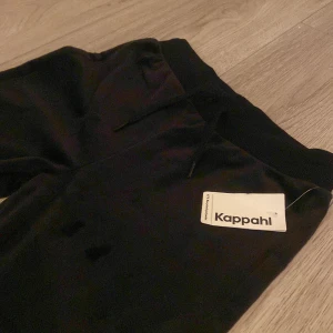Svarta bootcut mjukisbyxor Kappahl - Svarta mjukisbyxor från Kappahl med bootcut-ben och bred resår i midjan. Byxorna har snörning framtill och är gjorda i mjukt, lent material som känns skönt mot huden. Perfekta för chill dagar eller när du vill ha en avslappnad look.