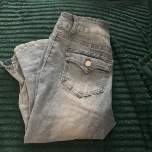 Ljusblå croppade jeansbyxor - Snygga ljusblå croppade jeansbyxor med hög midja och raka ben. Byxorna har dubbla framfickor och bakfickor med lock och knapp. De är tillverkade i mjukt jeansmaterial och har dragkedja och två knappar framtill. Perfekt för dig som gillar en chill och fräsch stil.