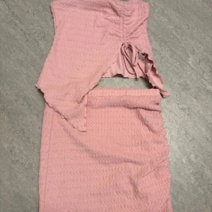 Rosa omlott sett med snörning - Säljer ett ljusrosa sett med omlott-design och snörning i midjan. Kjolen är mjuk och stretchig. Perfekt för dig som gillar trendiga och bekväma plagg med snygga detaljer.