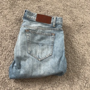 Blå jeans Tiger of Sweden 29/32 - Snygga ljusblå jeans från Tiger of Sweden i klassisk straight fit. Modellen har fem fickor, knapp och dragkedja framtill samt brunt läderpatch bak. Perfekt för dig som gillar stilrena och tidlösa jeans med modern vibe.