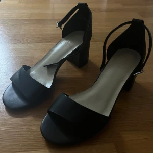 Svarta klackskor - Snygga svarta klackskor med bred rem över tårna och justerbar rem runt ankeln. Strl 36. Skorna har en stabil blockklack och öppen tå, vilket ger en stilren look o är enkla att gå i. Remen över tårna på höger fot har vikit sig lite, vilket syns på bild 4, dock inget som märks tydligt när man har på sig dem o går runt i dem 🥰blivit lite slitna längs kanterna på sulan, vilket syns på bild 4, dock inget som syns när foten är i ☺️ säljer då de blivit för små 💗