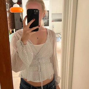 Vit prickig blus - Supersöt prickig vit blus, v-ringad hals och långa puffiga ärmar. Blusen har snörning i midjan och volangkant nedtill. Luftigt material som känns lätt och fräscht, perfekt för vår och sommar. Från stradivarius! Inga hål eller fläckar 