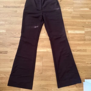 Bruna bootcut kostymbyxor - Snygga bruna kostymbyxor med bootcut-snitt och hög midja. Byxorna har klassisk form med raka ben som blir bredare nedtill och diskreta fickor framtill. Perfekta för dig som gillar en retrovibe och vill ha en stilren look.