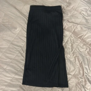 Svart långkjol från SHEIN XS - Snygg svart långkjol från SHEIN i storlek XS. Kjolen har ett stilrent, vertikalt randigt mönster och är gjord i mjuk polyester med lite stretch. Passformen är normal och kjolen har en diskret slits på sidan för extra rörelsefrihet.