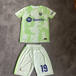 Barcelona old season kit ( REP) - Barcelona Lamine Yamal matchtröja med nummer 19 och shorts. Tröjan är ljusgrön med vita detaljer och har ett abstrakt mönster, korta ärmar och Dri-Fit-material. Tryck med Spotify och UNHCR-logga, samt klubbmärke på bröstet. Perfekt för dig som älskar fotboll och Barca.