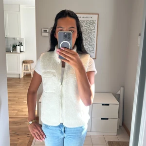 Vit fleeceväst med dragkedja - Säljer en fluffig vit fleeceväst med hög krage och hel dragkedja framtill. Västen har en cool ficka med dragkedja på bröstet och två sidofickor. Passformen är normal och materialet är mjuk. Köpt för tre år sedan och är lite noprig invändigt. Pris kan diskuteras.