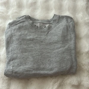 Grå sweatshirt från Cubus i XS - Säljer en enkel och stilren grå sweatshirt från Cubus i storlek XS. Tröjan har rund hals och är tillverkad i mjuk bomullsmix med ribbade muddar vid halsen. Perfekt för chill dagar eller när du vill ha en clean look.