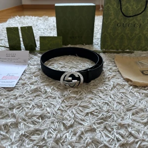 Svart GG bälte  - Säljer ett stilrent svart  bälte (kan ej skriva märket då annonsen tas bort men det står på lådorna) i skinn med präglat GG-mönster längs hela remmen. Bältet har ett stort, rundat spänne i blank silverfärg med den ikoniska GG-loggan. Perfekt accessoar för att lyfta din outfit med lyxig känsla och snygg detalj. Alla lådor och tags är kvar och medföljer bältet vid köp! 