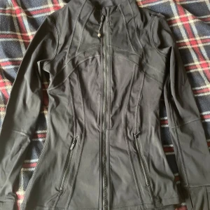 Svart träningsjacka från Lululemon - Snygg svart träningsjacka från Lululemon med figurnära passform, Storlek 4.