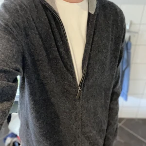 Kashmir tröja - Snygg mörkgrå cardigan jacka från Galeria i mjuk kashmir och silke. Jackan har lång ärm, hög krage och dragkedja framtill. Comfort fit för chill vibe och extra bekvämlighet. Perfekt för lager-på-lager under hösten och vintern.