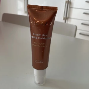 Hickap Bronze Glow Priming Moisturizer - Säljer en Hickap Bronze Glow Priming Moisturizer, en vegansk primer med bronzefärgad formula som ger glow och fukt. Tuben har pump och rymmer 50 ml. Passar alla hudtyper och innehåller hyaluronsyra för extra återfuktning. 