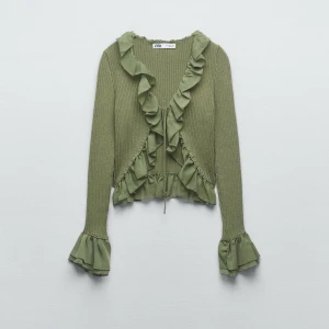 Grön kofta med volanger från Zara - Säljer en ljusgrön kofta från Zara med snygga volangdetaljer längs halsringningen, framkanten och ärmsluten. Koftan är ribbstickad, har lång ärm och knyt framtill. Perfekt att styla över ett linne eller t-shirt för en trendig look.