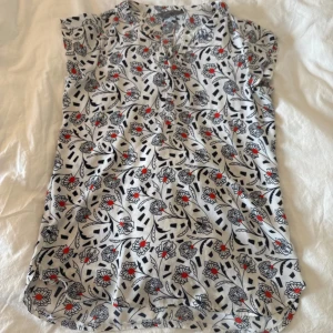 Blommig blus från Jacqui E, vit/röd - Säljer en blommig blus från Jacqui E i vit med svarta och röda detaljer. Blusen har korta ärmar, v-ringad hals och ett luftigt, normal passform. Materialet känns mjukt och lätt, perfekt för vår och sommar. Mönstret är riktigt coolt med röda blommor och svarta grafiska inslag.