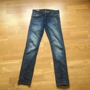 Slim fit jeans från Jack & Jones - Snygga blå jeans från Jack & Jones i modellen Slim/Glenn. De har en slim passform med klassisk femficksdesign och snygga slitningar på framsidan. Jeansen är tillverkade i jeansmaterial och har normal midja med knapp och dragkedja.