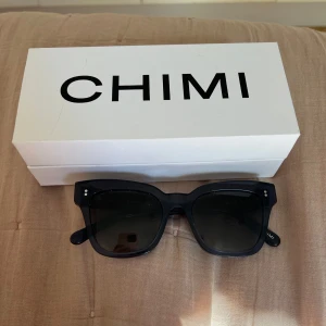 Blå CHIMI solglasögon med bred båge - Snygga solglasögon från CHIMI i mörkblå färg med bred, fyrkantig båge och svarta linser. Modellen är 07 BLUE P och har diskreta CHIMI-loggor på skalmarna samt två silverprickar vid bågfästet. Perfekt för dig som gillar stilrena accessoarer.