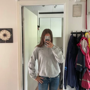 Grå hoodie ma cherie - Grå hoodie från Gina Tricot med coola stjärnmönster på ena ärmen och tryck på bröstet. Tröjan har snörning i halsen och ribbade muddar vid ärmslut och nederkant. Perfekt för dig som gillar en avslappnad och trendig stil.