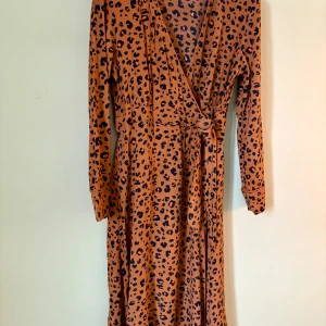 Leopardmönstrad omlottklänning & Other Stories - Säljer en långärmad omlottklänning från & Other Stories i storlek 42. Klänningen har ett snyggt leopardmönster i bruna och svarta toner, med knyt i midjan och v-ringad hals. 