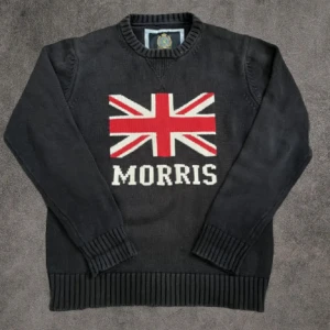 Svart stickad tröja Morris  - Svart stickad tröja från Morris i storlek Large med Union Jack-flagga och Morris-logga på bröstet. Tröjan har rund hals, ribbade muddar och är långärmad. Materialet är mjukt och skönt stickat, perfekt för kyliga dagar. Snygg och klassisk design med brittisk vibe.
