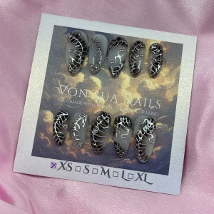 Z1NK (XS);Medium Almond - Handgjorda press-on naglar i storlek XS: 14 mm, 11 mm, 11,5 mm, 10 mm, 8 mm , med cool vit bas med svart dekor och silvriga, 3D mönster. Naglarna har en glansig finish och är dekorerade med små rhinestones för extra edge. Formen är medium almond och varje nagel är unik, perfekt för dig som vill sticka ut.