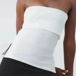 Vit bandeau tubtopp  - Snygg vit bandeau tubtopp med stilren och enkel design. Toppen är axelbandslös och har en lätt utsvängd nederkant som ger en cool siluett. Perfekt att matcha med jeans eller kjol för en fräsch look. Materialet känns mjukt och bekvämt mot huden.