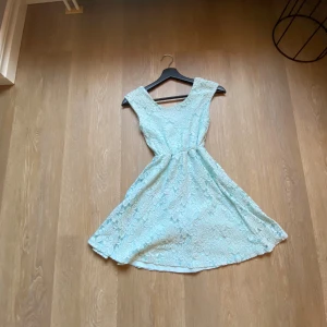 Ljusblå spetsklänning med blommönster - Säljer en söt ljusblå kortklänning med blommig spets och rundad halsringning. Klänningen är ärmlös och har en markerad midja som ger en fin siluett. Perfekt för sommarens alla tillfällen! Materialet är mjukt och luftigt, vilket gör den superbekväm att bära.