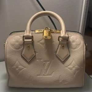 Beige Louis Vuitton handväska i skinn - Säljer en äkta Louis Vuitton väska i modellen speedy bandouliere 20 i färgen creme med guld detaljer. Köpt i Louis vutiiton butiken i Stockholm för 2 år sedan. Nypris 26000kr. Original box, dustbag, axelband och kvitto medföljer. Kan mötas upp i Stockholm. 💗💗 kan gå ner i pris vid snabb affär
