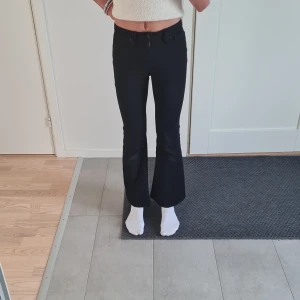 Svarta flare jeans från Vailent - Snygga svarta jeans från Vailent med flare-ben och hög midja. Modellen har klassiska fem fickor, knapp och dragkedja framtill. Jeansen är i stretchigt material. Jag är ca 170 och de här jeansen är lite för små/korta.