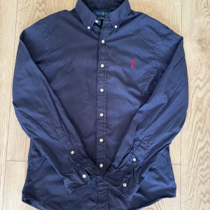 Mörkblå skjorta från Ralph Lauren - Snygg mörkblå skjorta från Ralph Lauren i slim fit, strl M. Skjortan är använd men i fint skick. Pris är diskuterandet vid snabb affär! Tveka inte på att höra av dig om du har frågor!