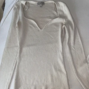 Vit ribbad långärmad topp H&M - Säljer en vit ribbad topp från H&M med lång ärm och snygg v-ringad hals. Modellen är slim och sitter tajt mot kroppen, perfekt för dig som gillar en clean och stilren look. Materialet är mjukt och stretchigt, vilket gör den skön att bära hela dagen.