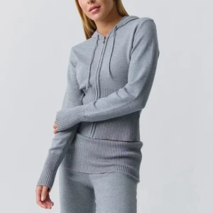 Grå hoodie med dragkedja och huva - Snygg grå hoodie med dragkedja och huva, ribbad midja och ärmslut. Tröjan har snörning vid huvan och är långärmad. Materialet är stickat och känns mjukt mot huden, perfekt för chill dagar. Passformen är normal och färgen är ljusgrå.