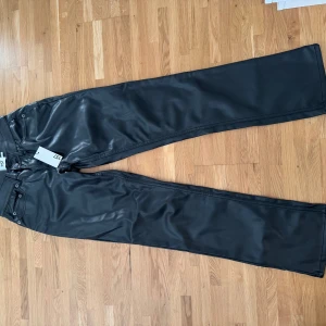 Svarta wide byxor i skinn från 157 - Snygga svarta byxor från 157 i skinnimitation med breda ben och klassisk femficksdesign. Byxorna har hög midja och raka sömmar, vilket ger en cool och modern vibe. Perfekta för dig som vill sticka ut med en edgy look.