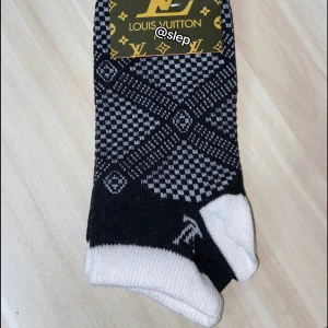 Svarta Louis Vuitton strumpor - Snygga strumpor från Louis Vuitton med schackrutigt mönster i svart och vitt. De har den klassiska LV-loggan vid ankeln och är låga i modellen. Perfekta för dig som vill ha en lyxig touch på din outfit.