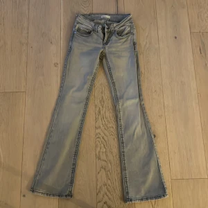 Bootcut ljusgrå jeans från Perfect Jeans - Snygga ljusgrå bootcut jeans från Perfect Jeans i storlek 34. Klassisk femficksdesign med bälteshällor och dragkedja. Jeansen har en mjuk tvättad look och är tillverkade i jeansmaterial som sitter skönt. Perfekt för dig som gillar retrovibbar och vill sticka ut.